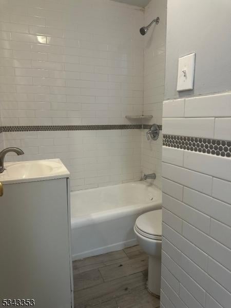 bathroom with tile walls, toilet, bathing tub / shower combination, wood finished floors, and vanity