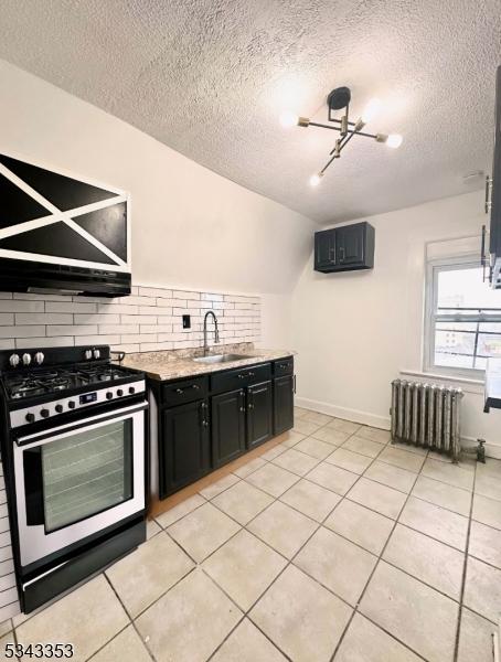 kitchen featuring dark cabinetry, radiator, gas stove, a sink, and backsplash