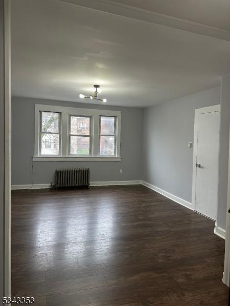 spare room with baseboards, radiator, and dark wood finished floors