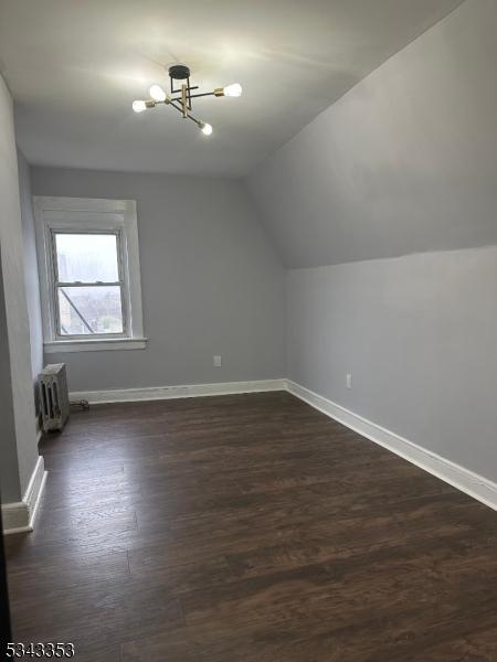 additional living space with vaulted ceiling, radiator, baseboards, and dark wood-style flooring