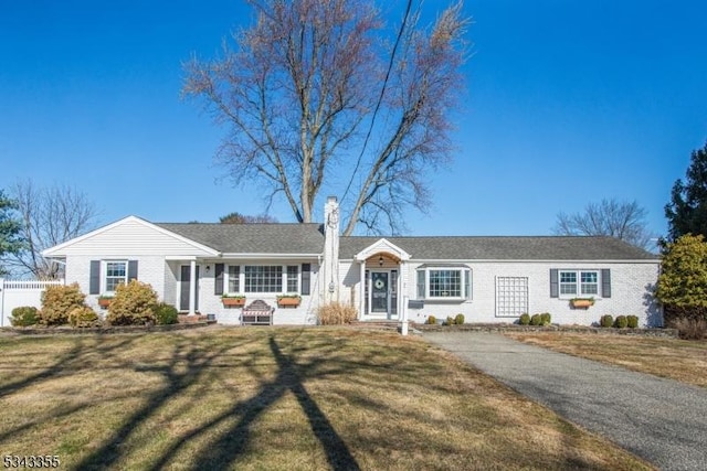 ranch-style home featuring brick siding, a chimney, a front lawn, and fence