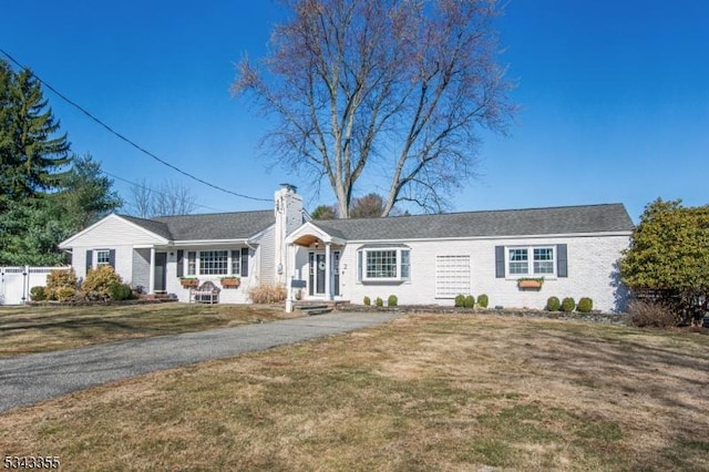 ranch-style home featuring brick siding, a chimney, a front lawn, and fence