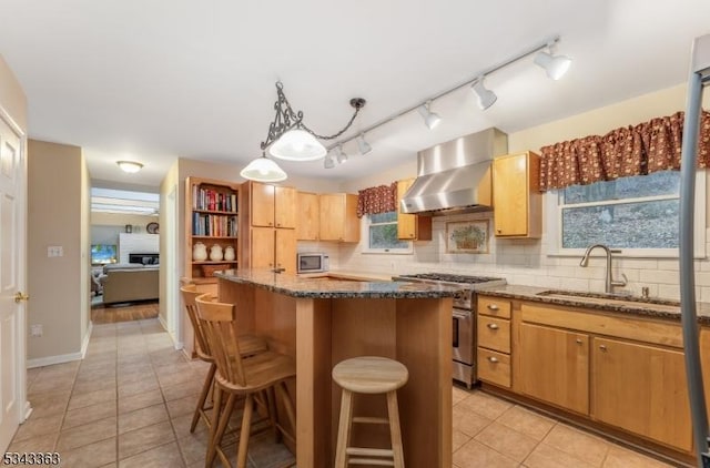 kitchen featuring a kitchen island, wall chimney range hood, decorative backsplash, appliances with stainless steel finishes, and a sink