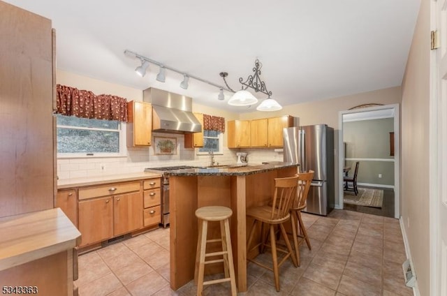 kitchen featuring a sink, appliances with stainless steel finishes, wall chimney range hood, tasteful backsplash, and a center island