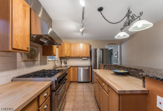 kitchen with backsplash, appliances with stainless steel finishes, wall chimney exhaust hood, butcher block counters, and light tile patterned floors