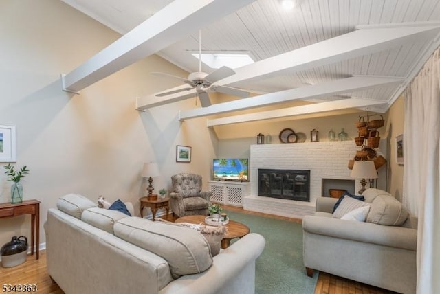 living area featuring vaulted ceiling with skylight, a fireplace, ceiling fan, and wood finished floors