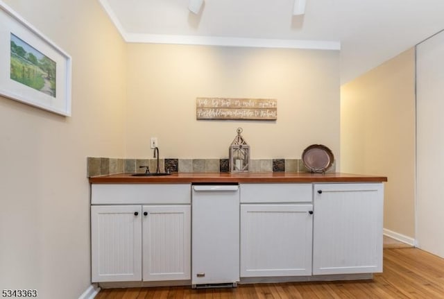 bar with light wood-type flooring, ornamental molding, a sink, indoor wet bar, and baseboards