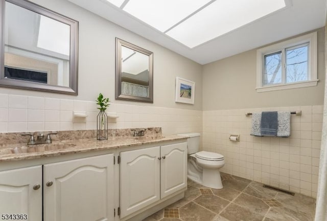 bathroom featuring visible vents, toilet, vanity, wainscoting, and tile walls