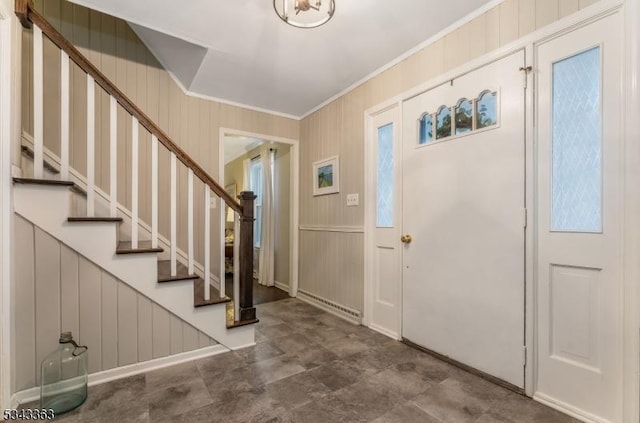 foyer featuring stairs, crown molding, wooden walls, and baseboard heating