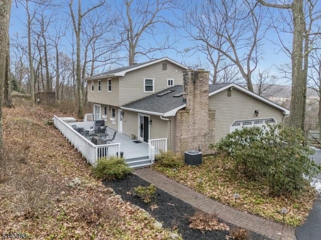 view of front of property featuring central AC unit, a wooden deck, a shingled roof, a chimney, and a garage