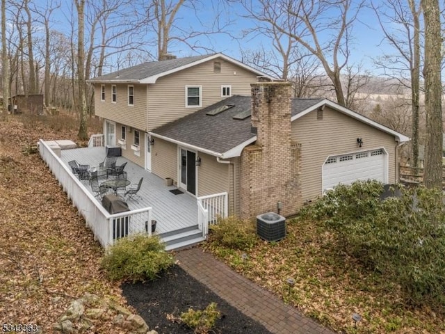 view of side of property with roof with shingles, an attached garage, a wooden deck, central AC unit, and a chimney