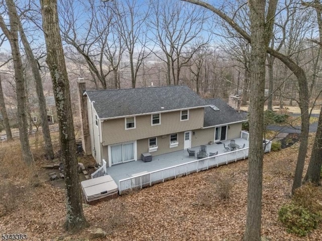 rear view of house with a chimney, a deck, and a shingled roof