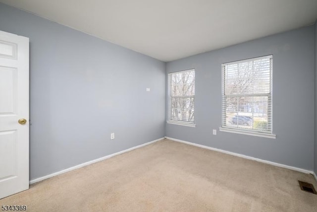 spare room featuring visible vents, light colored carpet, and baseboards