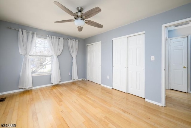 unfurnished bedroom featuring light wood finished floors, visible vents, two closets, and baseboards