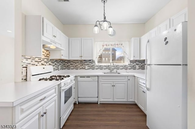 kitchen with under cabinet range hood, dark wood finished floors, decorative backsplash, white appliances, and a sink