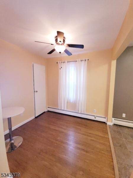 spare room with a baseboard heating unit, wood finished floors, baseboards, and ceiling fan