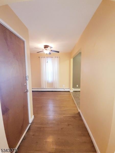 hallway featuring baseboard heating, baseboards, and wood finished floors