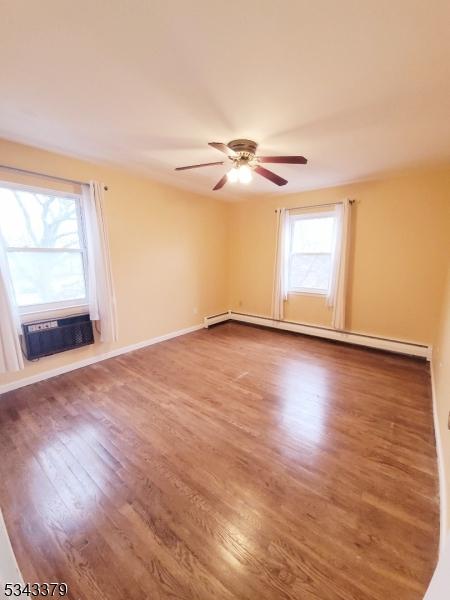 unfurnished room with a wealth of natural light, baseboard heating, a wall unit AC, and wood finished floors