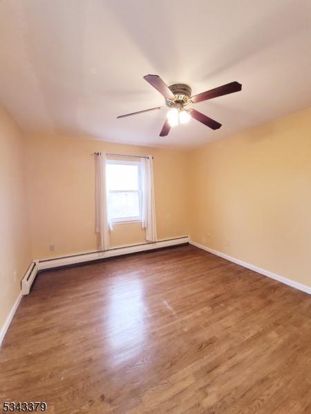 spare room with wood finished floors, baseboards, and a baseboard radiator