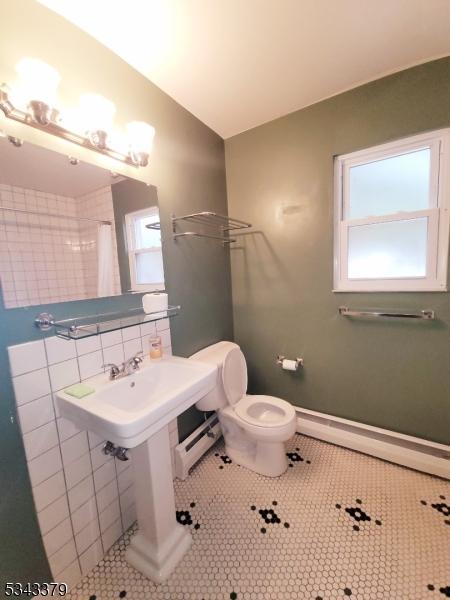 bathroom featuring decorative backsplash, baseboard heating, a healthy amount of sunlight, and tile patterned flooring