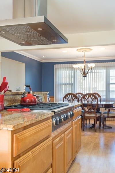 kitchen with crown molding, light stone countertops, light wood-type flooring, an inviting chandelier, and stainless steel gas stovetop