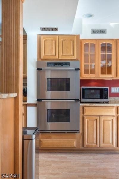 kitchen featuring light wood-type flooring, visible vents, light brown cabinets, stainless steel appliances, and glass insert cabinets