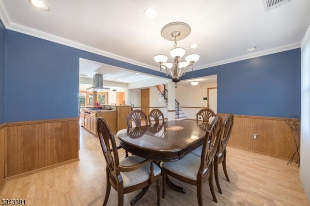 dining room with a wainscoted wall, light wood-style flooring, an inviting chandelier, and ornamental molding