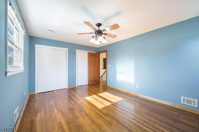 unfurnished bedroom featuring a ceiling fan, wood finished floors, visible vents, and multiple closets