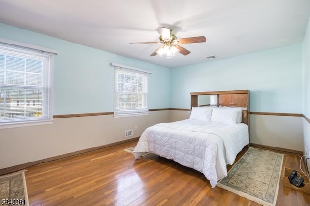 bedroom with visible vents, a ceiling fan, baseboards, and wood finished floors