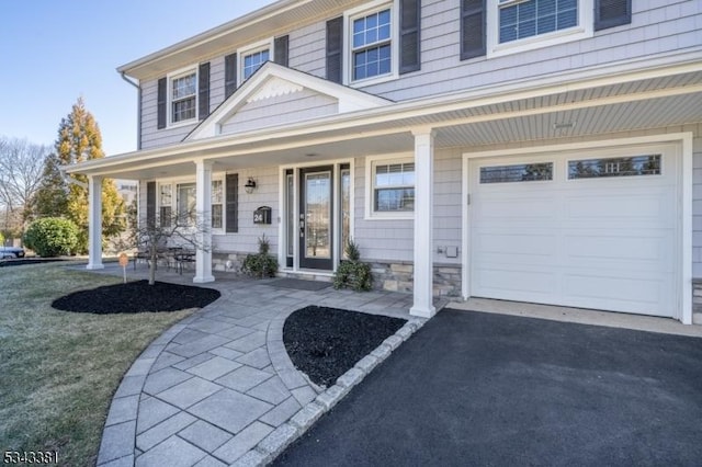 entrance to property with aphalt driveway, stone siding, covered porch, and a garage