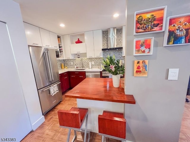 kitchen featuring stainless steel appliances, white cabinetry, wall chimney exhaust hood, backsplash, and butcher block counters