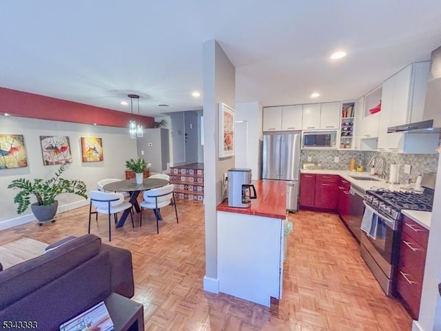 kitchen featuring a sink, decorative backsplash, stainless steel appliances, white cabinets, and wall chimney range hood