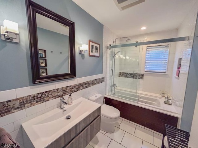 bathroom featuring tile patterned floors, toilet, tiled shower / bath combo, tile walls, and vanity