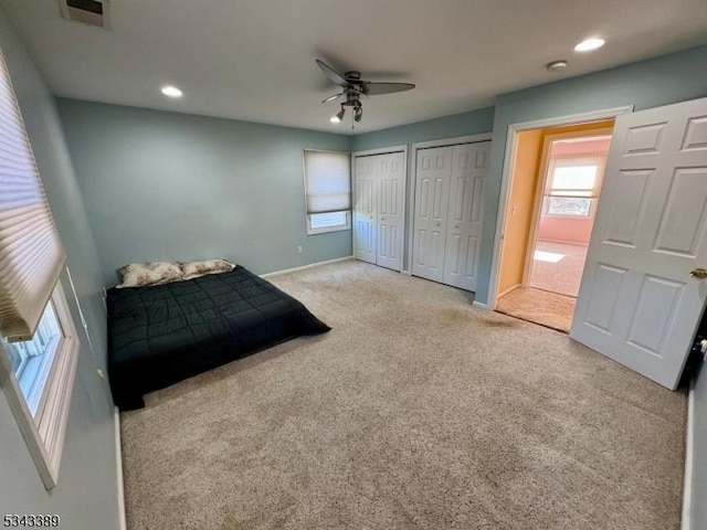 carpeted bedroom with visible vents, multiple windows, two closets, and baseboards