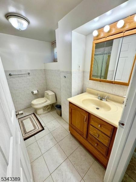 bathroom with tile patterned flooring, tile walls, a wainscoted wall, toilet, and vanity