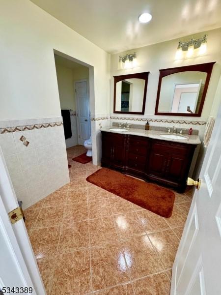 bathroom featuring double vanity, wainscoting, tile walls, and a sink