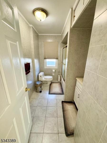 full bathroom with tile patterned floors, toilet, tile walls, and crown molding