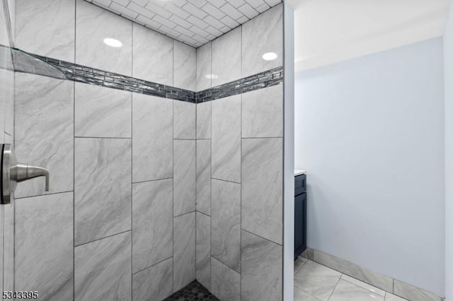 bathroom with baseboards, tiled shower, and vanity