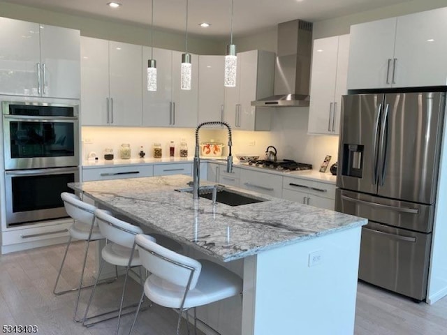 kitchen with a sink, wall chimney range hood, light wood finished floors, and stainless steel appliances