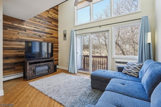 living area featuring baseboard heating, a towering ceiling, wooden walls, and wood finished floors