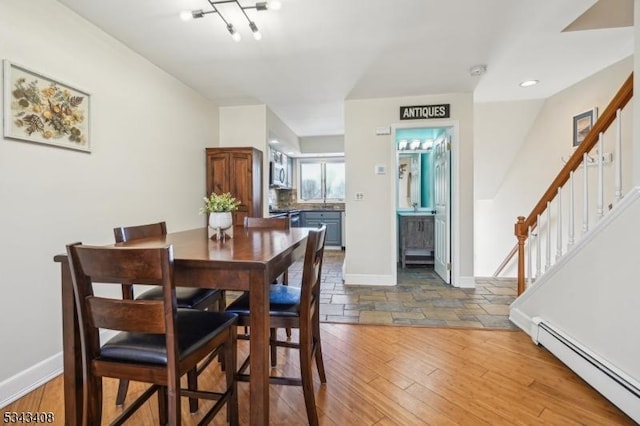 dining area featuring stairway, a baseboard heating unit, baseboards, and wood finished floors