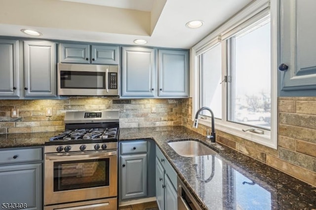 kitchen featuring decorative backsplash, dark stone countertops, gray cabinets, appliances with stainless steel finishes, and a sink