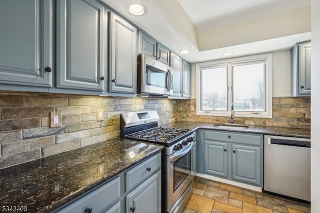 kitchen featuring gray cabinets, a sink, stone tile flooring, stainless steel appliances, and decorative backsplash