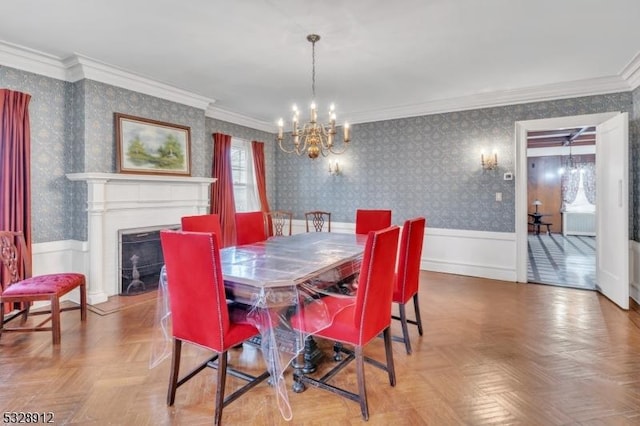 dining space with a wainscoted wall, a chandelier, crown molding, and wallpapered walls