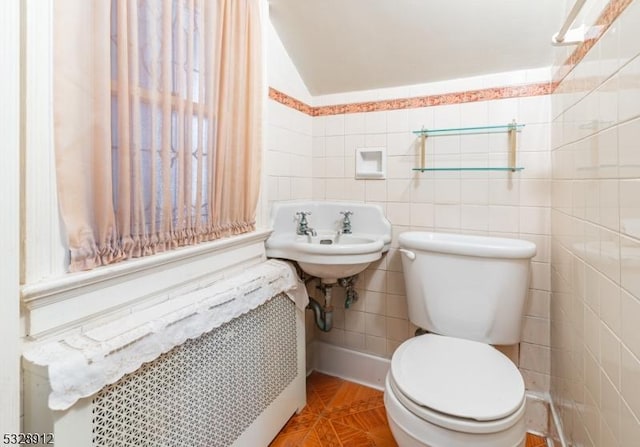 bathroom with toilet, radiator, tile walls, and a sink