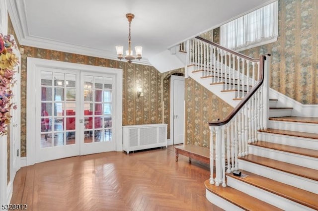 foyer entrance featuring a notable chandelier, radiator heating unit, french doors, crown molding, and wallpapered walls