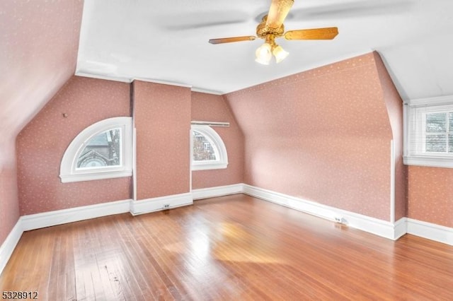 additional living space featuring a ceiling fan, wood finished floors, wallpapered walls, baseboards, and vaulted ceiling