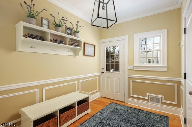 doorway to outside with a decorative wall, light wood-style floors, visible vents, and ornamental molding