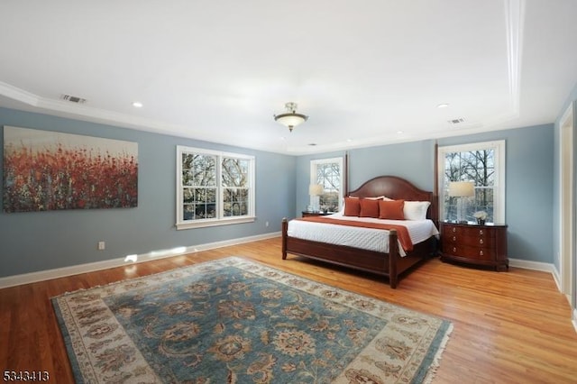 bedroom featuring wood finished floors, crown molding, baseboards, and visible vents