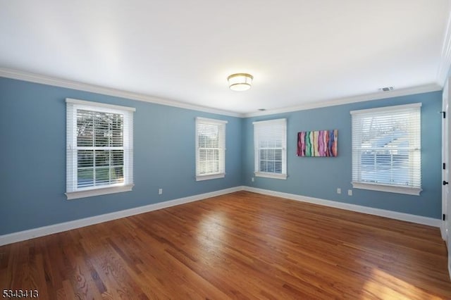 unfurnished room with visible vents, baseboards, wood finished floors, and crown molding